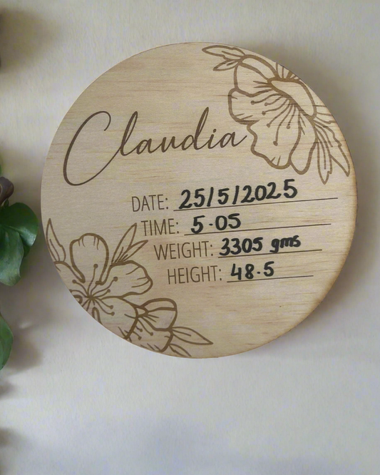 Wooden disc with engraved baby details and floral designs on a white background.